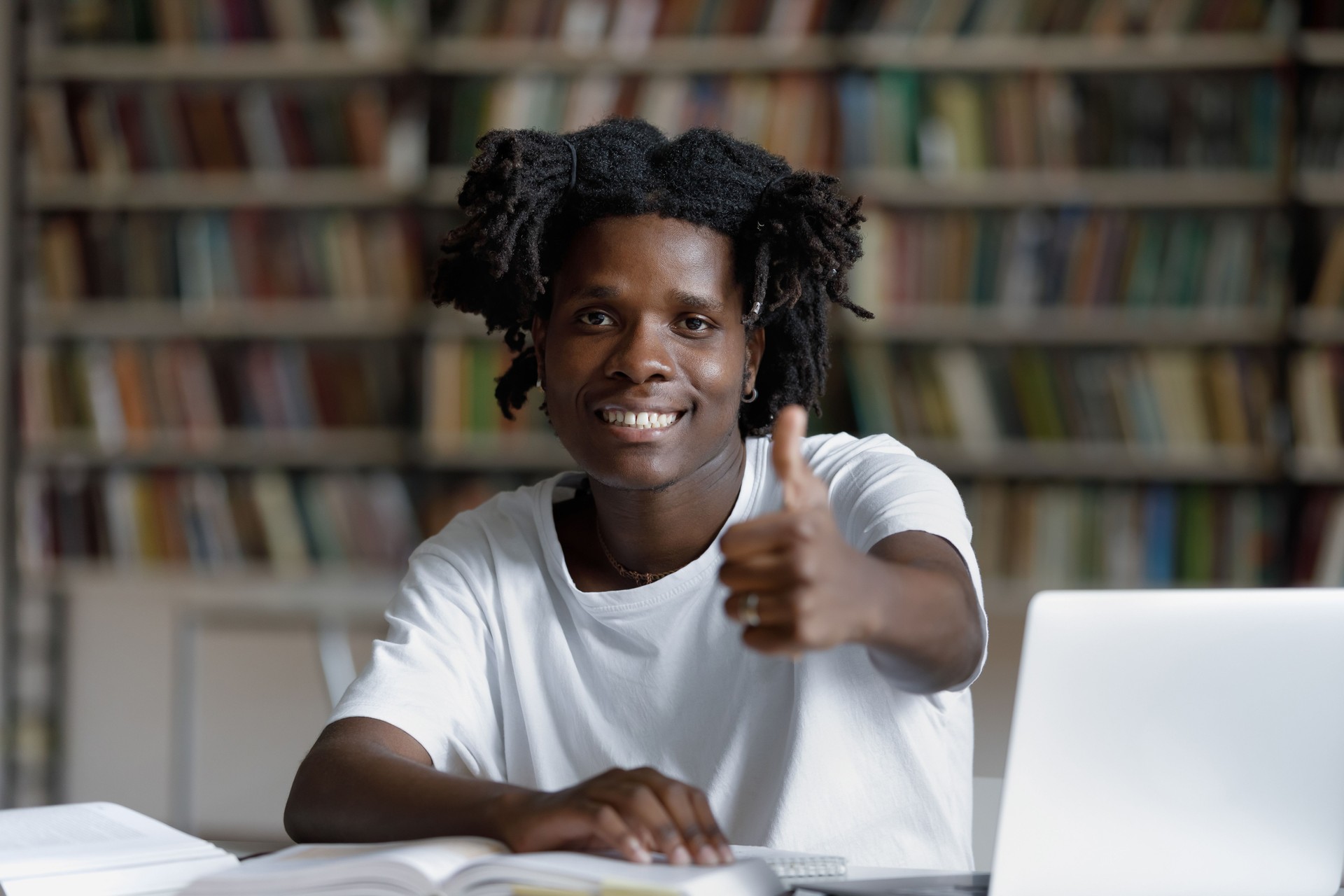 African student sit at desk in library showing thumbs up